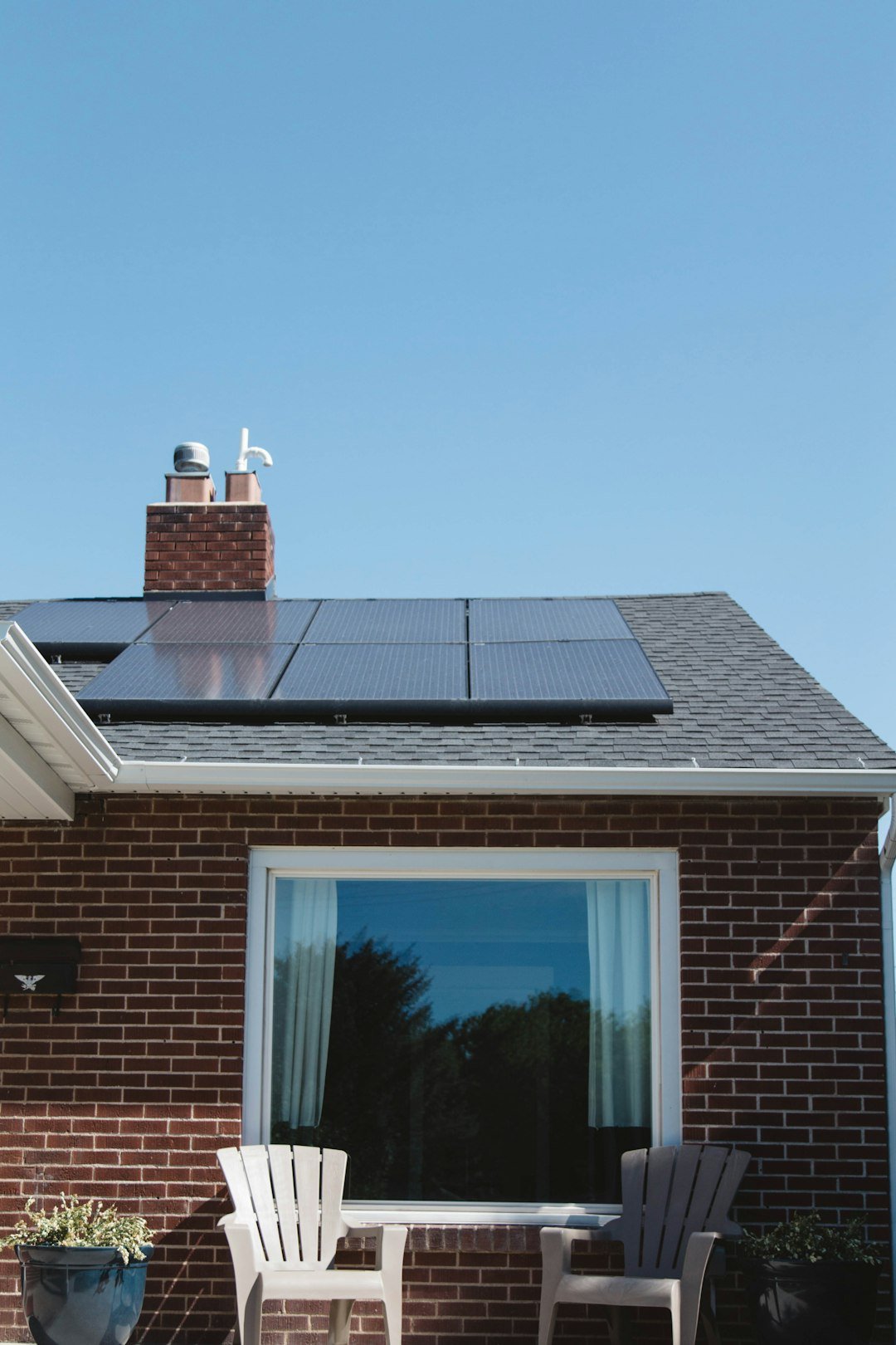 services-01 Vivint Solar - Solar Panels on roof of brick home with window and Adirondack chairs.